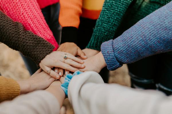 A number of people in a circle all placing their hands in the centre