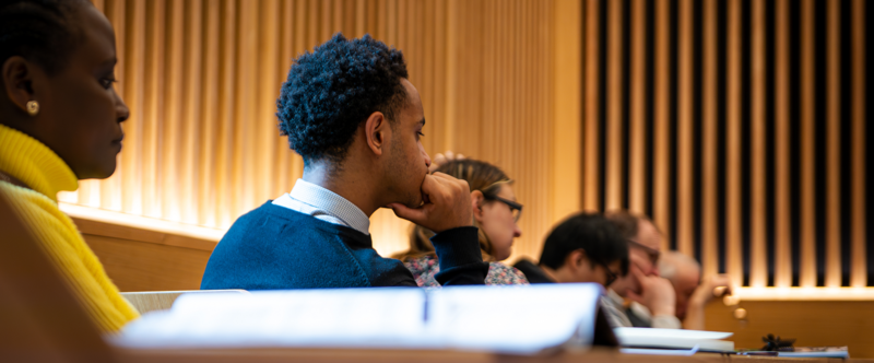 A group of students sit in a lecture theatre listening 