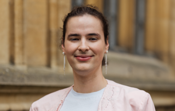 Addi Haran Diman stands with in front of buildings in Radcliffe Square wearing a light peach shirt