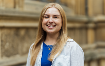 Lauren Schaefer standing in front of college buildings in Radcliffe Square wearing a blue shirt