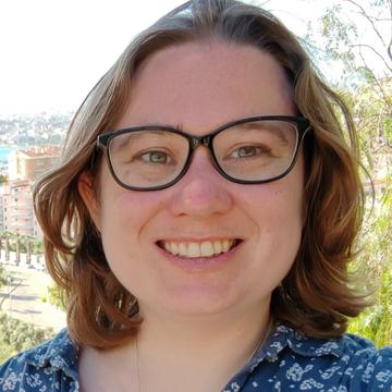 Joanna smiling against a sunny background, wearing glasses and a blue floral shirt. 