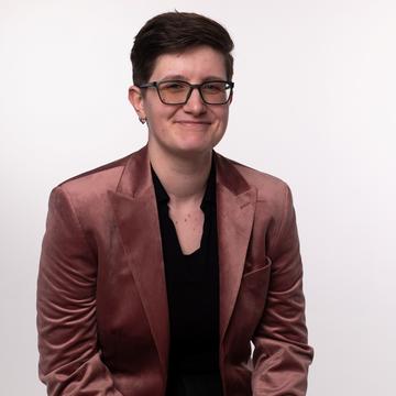 Maddie wearing a black shirt and auburn jacket against a plain background. 