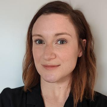 An image of Steph Perrin smiling against a plain background, wearing a black shirt. 